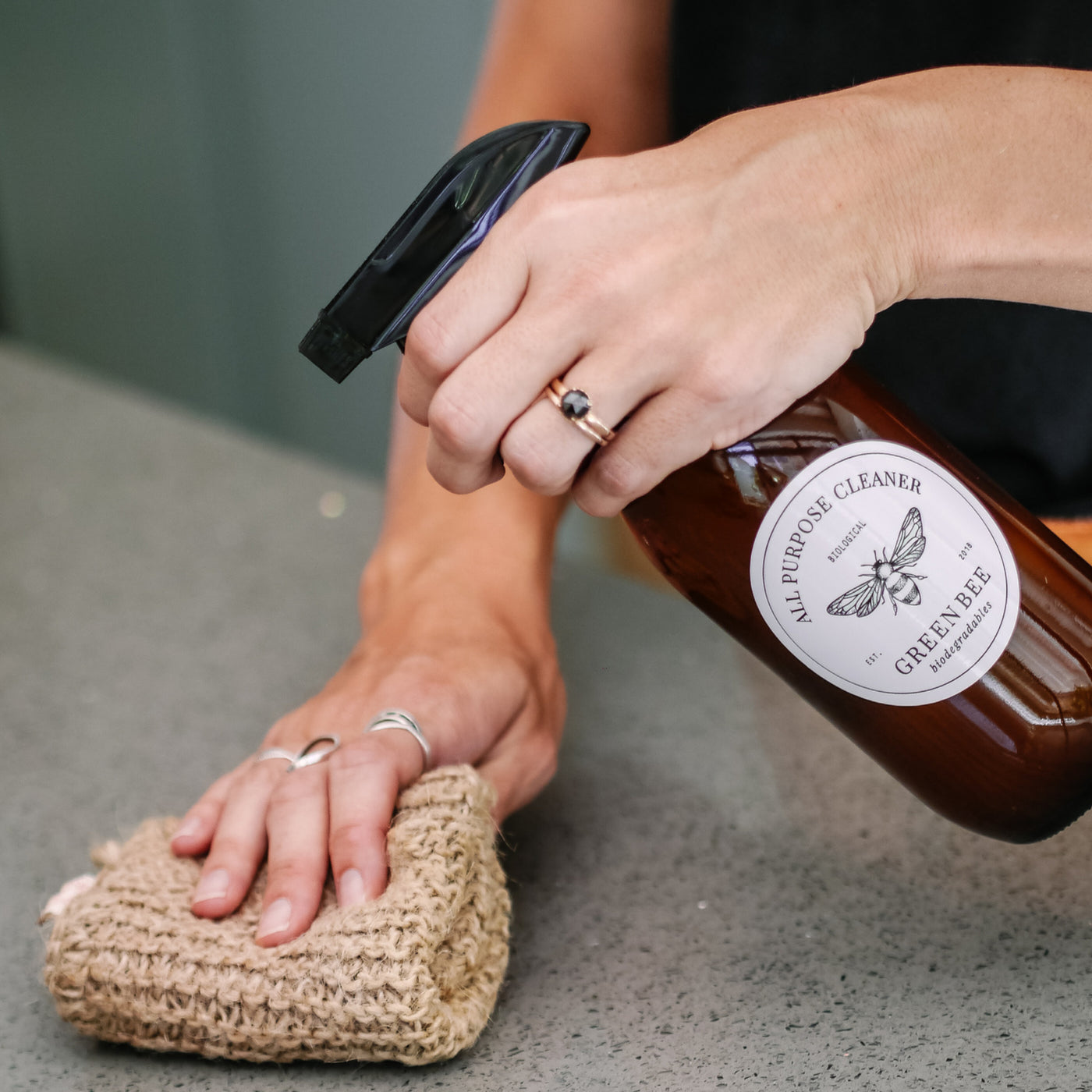 Hands wiping a kitchen counter with Green Bee All Purpose Cleaner